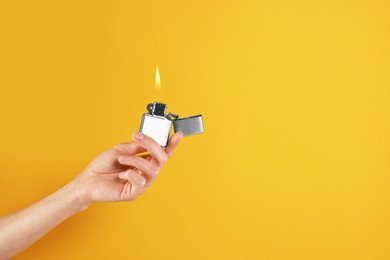 Photo of Woman holding lighter with burning flame on orange background, closeup. Space for text