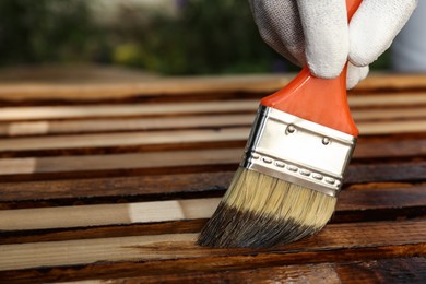 Worker applying wood stain onto planks outdoors, closeup. Space for text