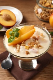 Photo of Tasty peach yogurt with granola, mint and pieces of fruit in dessert bowl on wooden table