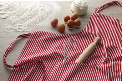 Photo of Red striped apron with kitchen tools and different ingredients on wooden table