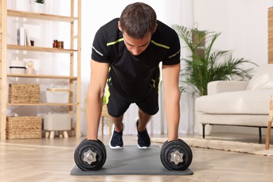 Handsome man doing plank exercise with dumbbells on floor at home
