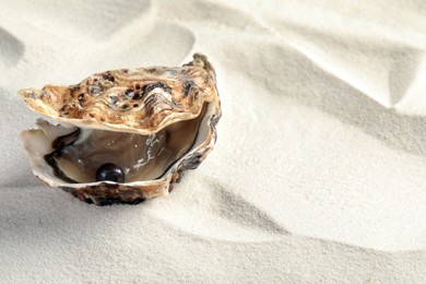 Open oyster with black pearl on sand, space for text