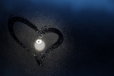 Glass with heart drawn in condensation against dark background. Space for text