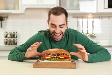 Young hungry man and tasty sandwich in kitchen