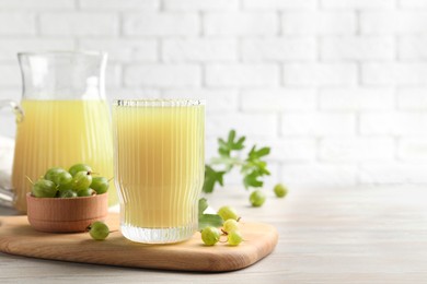 Tasty gooseberry juice and fresh berries on light wooden table. Space for text