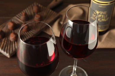 Glasses of red wine with chocolate candies on wooden table, closeup