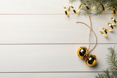 Golden sleigh bells, serpentine streamers and fir branches on white wooden background, flat lay. Space for text