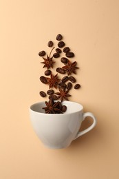 Photo of Coffee beans and anise stars falling into cup on beige background, flat lay
