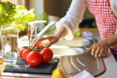 Woman with fresh tomatoes at countertop in kitchen, closeup