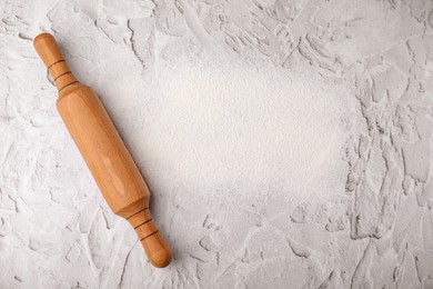 Flour and rolling pin on white textured table, top view