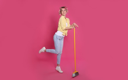 Young housewife with broom on pink background