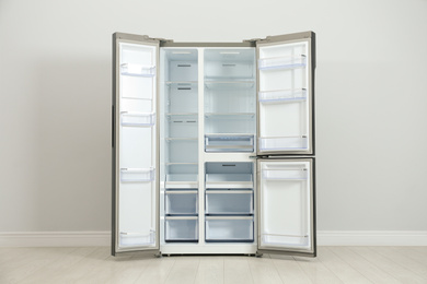 Modern empty refrigerator near light grey wall. Home appliance