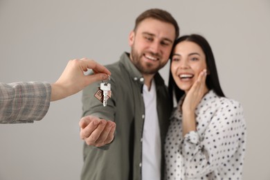 Real estate agent giving key to happy young couple against grey background, focus on hands