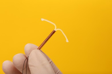 Doctor holding T-shaped intrauterine birth control device on yellow background, closeup