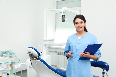 Portrait of professional female dentist with clipboard in clinic. Space for text