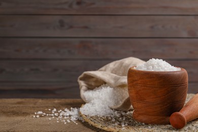 Pestle and mortar with natural sea salt on wooden table, space for text