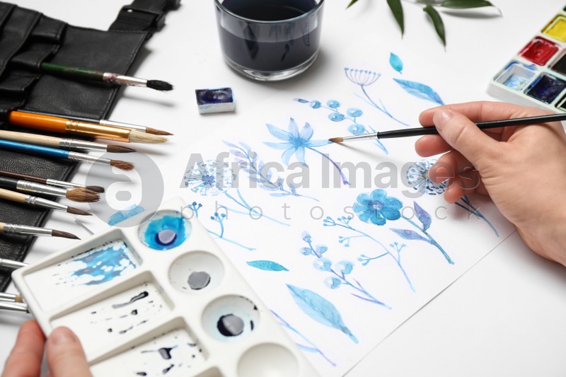 Woman painting flowers with watercolor at white table, closeup