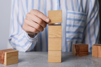 Photo of Woman stacking wooden cubes at table, closeup. Management concept