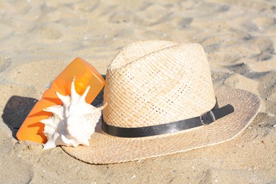Stylish straw hat, sea shell and sunscreen on sandy beach