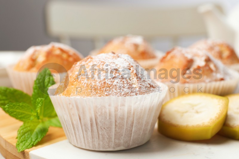Photo of Tasty muffins served with mint and banana on board, closeup