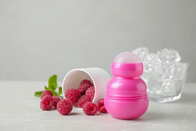 Female roll-on deodorant with raspberries and ice on light grey table