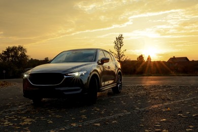 Photo of Black modern car parked on road at sunset