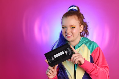 Photo of Cute indie girl with VHS cassette on violet background, space for text