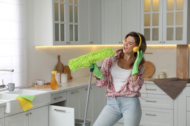 Photo of Beautiful young woman with headphones singing while cleaning kitchen