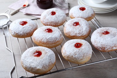 Many delicious donuts with jelly and powdered sugar on cooling rack