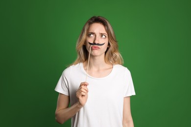 Thoughtful woman with fake mustache on green background