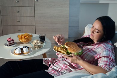 Happy overweight woman eating french fries with burgers at home