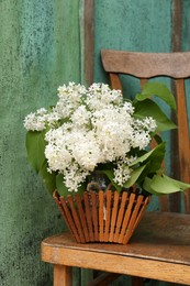 Photo of Beautiful lilac flowers in wooden basket near green wall