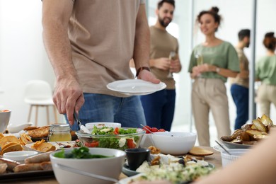 Photo of Man with plate taking salad from buffet indoors, closeup. Brunch table setting