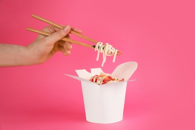 Woman eating vegetarian wok noodles with chopsticks from box on pink background, closeup