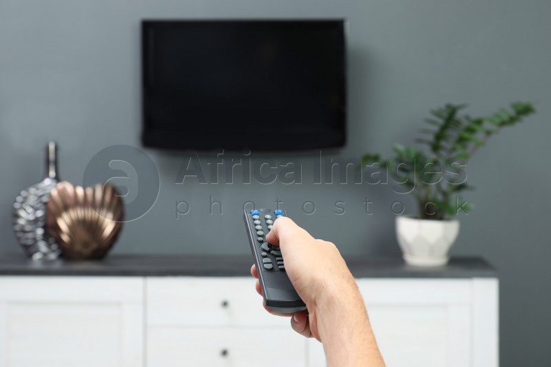 Photo of Man switching channels on plasma TV with remote control at home