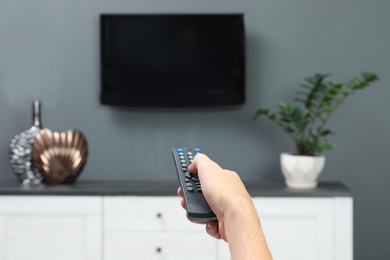 Man switching channels on plasma TV with remote control at home