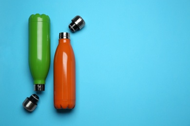 Modern thermo bottles on light blue background, flat lay. Space for text