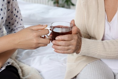 Caregiver giving tea to elderly woman at home, closeup