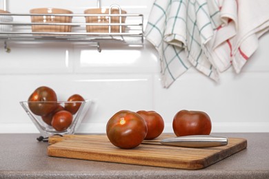 Wooden board with knife and tomatoes on kitchen table