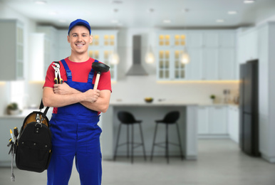 Young plumber with tool bag in kitchen, space for text