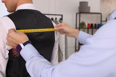 Professional tailor measuring client's back width in atelier, closeup