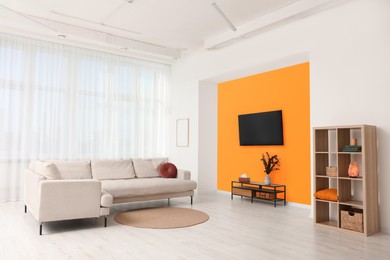 Photo of Stylish sofa and wooden furniture near orange wall in spacious room. Interior design