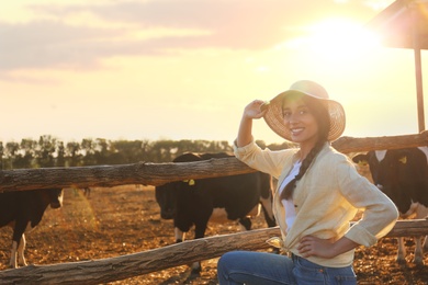 Young woman standing near cow pen on farm. Animal husbandry