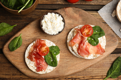 Puffed rice cakes with prosciutto, tomato and basil on wooden table, flat lay