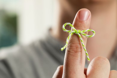 Man showing index finger with tied bow as reminder against blurred background, focus on hand