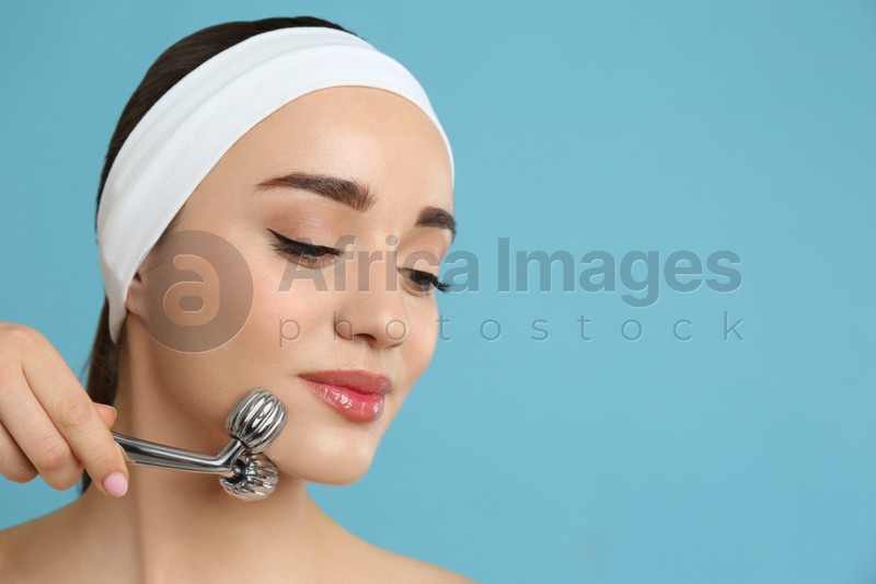 Photo of Woman using metal face roller on light grey  background, space for text