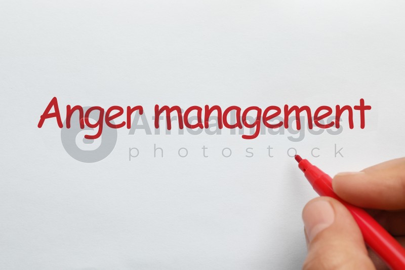 Photo of Man writing phrase Anger Management with red felt tip pen on white paper, top view