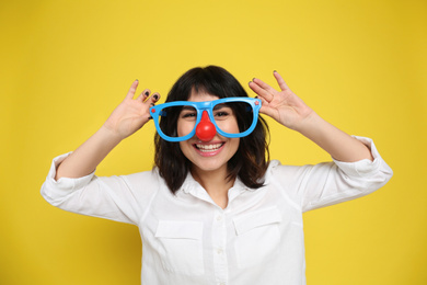 Photo of Joyful woman with funny glasses on yellow background. April fool's day
