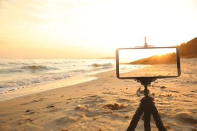 Taking photo of beautiful sandy beach with smartphone mounted on tripod