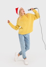 Photo of Emotional woman in Santa Claus hat singing with microphone on light grey background. Christmas music